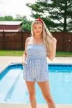 Woman with a red headband and blue gingham romper standing by a pool with trees in the background.