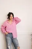 Woman in pink shirt and distressed jeans posing against a white wall.