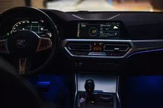 Interior view of a car featuring the steering wheel, dashboard, and infotainment system illuminated by blue ambient lighting.
