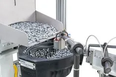 Robotic arm sorting screws in an industrial feeder system.