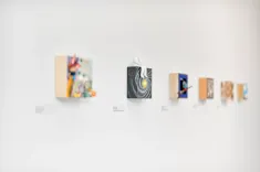 Art gallery wall with a series of blurred artworks and a focused painting featuring a spiral galaxy with a sculptural white figure on top.
