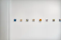 Art gallery wall showcasing a variety of small contemporary artworks with description labels underneath each piece.
