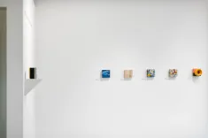 Modern art exhibit with various small framed pieces displayed on a white gallery wall.