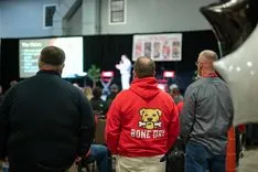 Attendees at a conference viewed from behind, focusing on a person in a red jacket with a 'Gone Dog' logo.