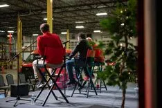 People sitting on chairs in a warehouse-like setting participating in an event, viewed from behind a plant.