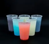 Six transparent plastic cups filled with colorful liquids arranged in a row on a black background.