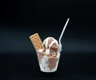 Chocolate and vanilla ice cream in a cup with a biscuit and a plastic spoon on a black background.