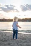 Toddler standing on the beach at sunset looking out at the water.