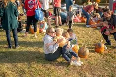 People enjoying a pumpkin patch event on a sunny day with various activities in the background.