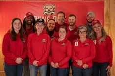 Group of people wearing red shirts smiling in front of a banner with a bear mascot logo.