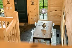 Cozy dining area with a wooden table and chairs inside a cabin with pine walls and a glass door leading outside.