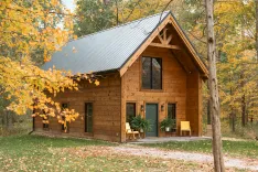 A cozy wooden cabin with a green door surrounded by autumn foliage in a forest setting.