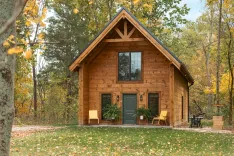 Wooden cabin with large windows surrounded by autumn foliage.