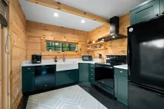 Rustic style kitchen interior with natural wood walls and ceiling, featuring dark green cabinets, modern appliances, a white farmhouse sink, and hexagonal tile flooring.