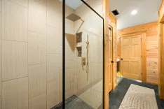 Modern bathroom interior with glass shower, tiled walls, and wooden door leading to sauna.