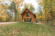 A cozy wooden cabin surrounded by autumnal trees with fallen leaves on the ground.