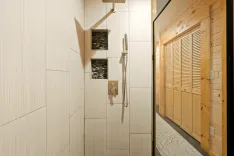 Modern bathroom interior with a wooden sauna cabin, beige tiled walls, and shower accessories including a rainfall showerhead.