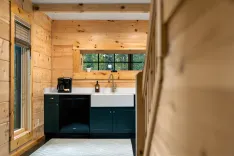 A cozy wooden kitchen interior with a large window, white countertops, and dark green cabinets.