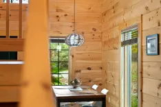 Cozy wooden cabin interior with dining table set, modern pendant lamp, and view of nature through window.