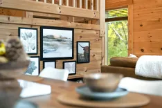 Cozy wooden cabin interior with art on walls, stair railing, comfy furniture, and a view of trees through the window.