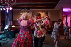Couples dancing together in a dimly lit room with a chandelier and a live music setup in the background.