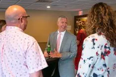 Group of people conversing with a smiling man in a gray suit at a social event.