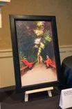 Painting displayed on an easel featuring abstract figures in red dresses with a blurred background suggesting movement or light play.