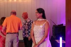 Woman smiling at social event with people dancing in the background.