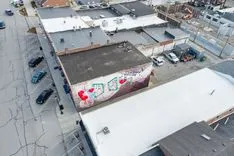 Aerial view of an urban area showing the rooftops of industrial buildings, some with graffiti, and parking lots with cars.