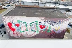 Aerial view of a rooftop with a colorful graffiti mural, set against an urban backdrop.
