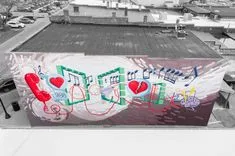 Colorful mural on a building's facade in an urban environment, with musical and heart symbols, in a black and white cityscape.