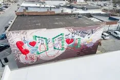 Aerial view of a rooftop with a colorful mural spelling "LOVE" with each letter designed uniquely, surrounded by urban scenery.