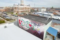 Aerial view of an urban area with a building featuring a colorful graffiti mural in the foreground and a historic courthouse in the background.